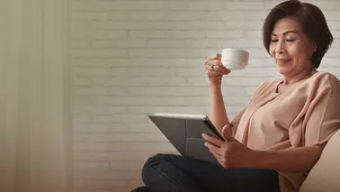 Femme assis qui regarde une tablette et avec une tasse